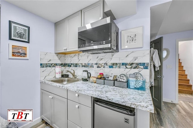 kitchen with light hardwood / wood-style floors, sink, light stone countertops, and decorative backsplash