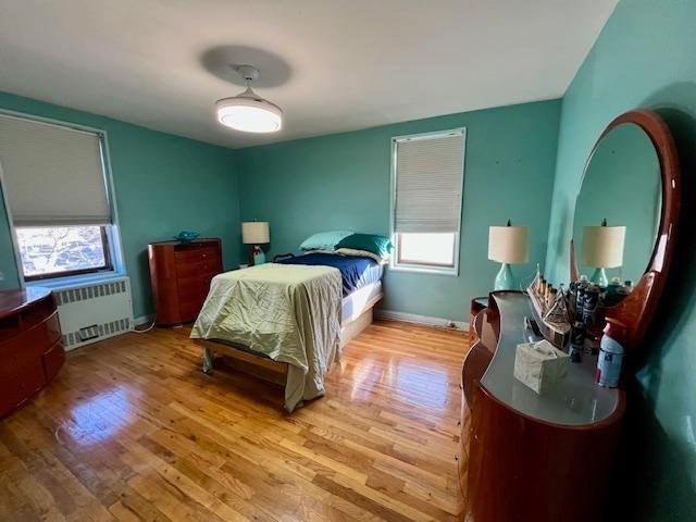 bedroom with radiator heating unit, wood finished floors, and baseboards
