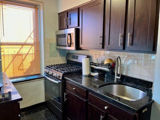 kitchen with decorative backsplash, appliances with stainless steel finishes, dark stone countertops, and sink