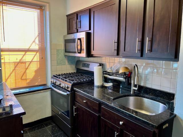 kitchen featuring appliances with stainless steel finishes, a sink, decorative backsplash, and dark stone counters