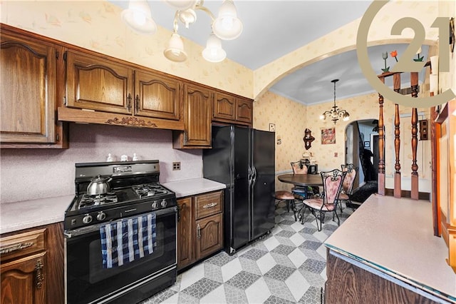 kitchen featuring wallpapered walls, arched walkways, light countertops, black appliances, and a chandelier