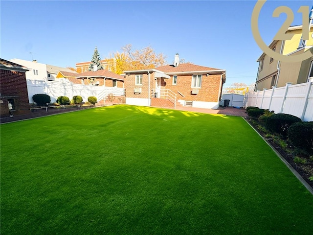 back of house featuring brick siding, a fenced backyard, and a yard