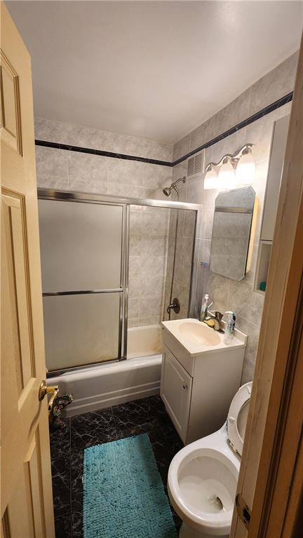 bathroom with vanity, enclosed tub / shower combo, and tile walls