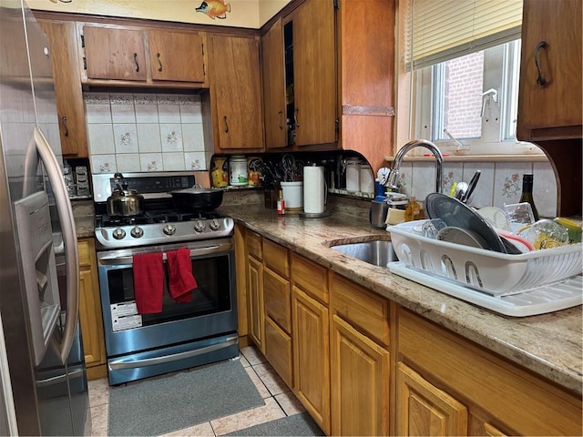 kitchen featuring decorative backsplash, appliances with stainless steel finishes, light stone countertops, sink, and light tile patterned floors