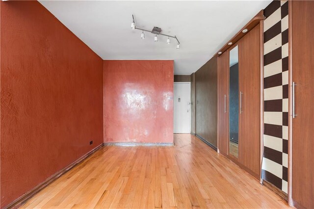 empty room with track lighting and light hardwood / wood-style flooring