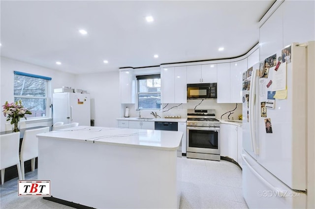 kitchen with sink, white cabinetry, light stone counters, black appliances, and a kitchen island