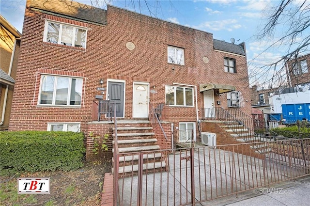 multi unit property featuring ac unit, brick siding, and a fenced front yard