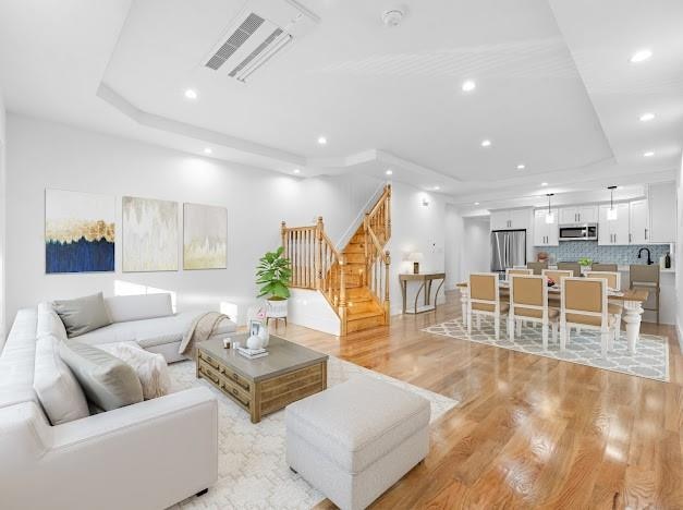 living room with light hardwood / wood-style floors and a raised ceiling