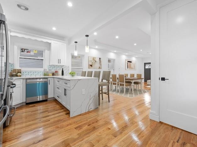 kitchen with kitchen peninsula, backsplash, dishwasher, hanging light fixtures, and white cabinets