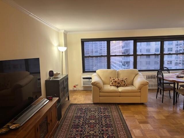 living room featuring radiator heating unit, ornamental molding, a wall mounted AC, and light parquet floors