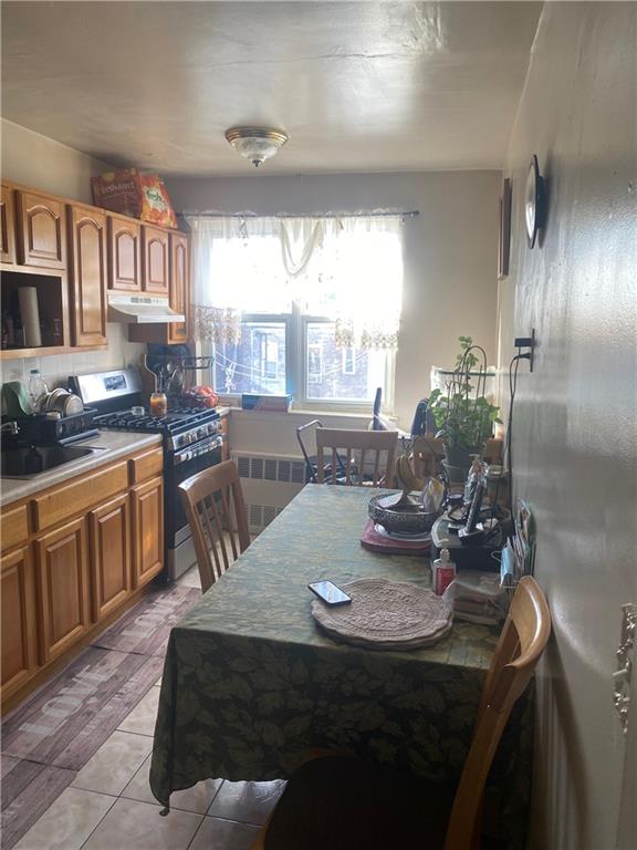 kitchen with light tile patterned floors, radiator heating unit, sink, and stainless steel gas range oven