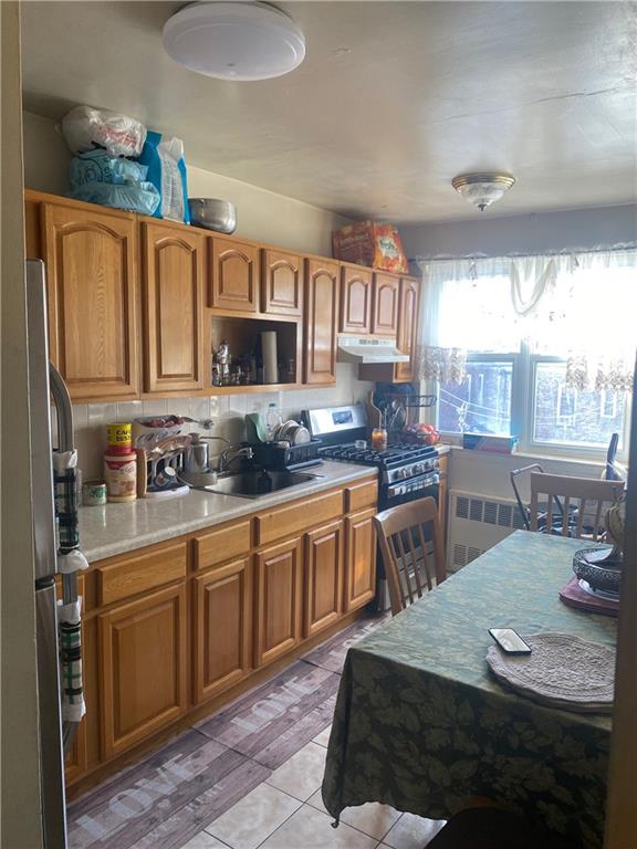 kitchen featuring radiator, sink, light tile patterned floors, tasteful backsplash, and stainless steel appliances