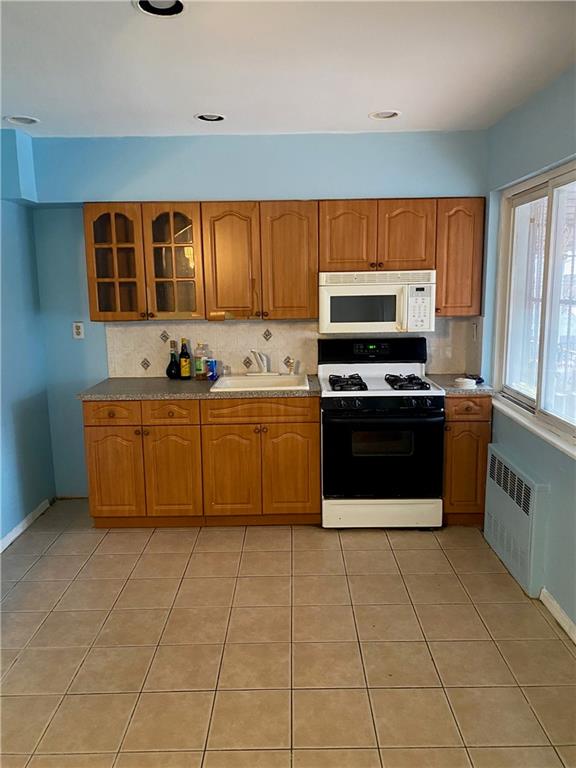 kitchen with radiator heating unit, light tile patterned floors, white appliances, and sink