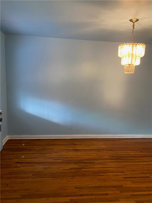 unfurnished room featuring a chandelier and dark wood-type flooring