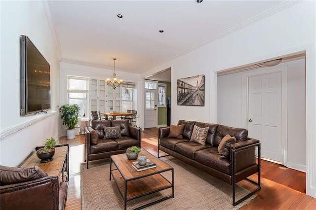 living room featuring ornamental molding, wood-type flooring, and a notable chandelier