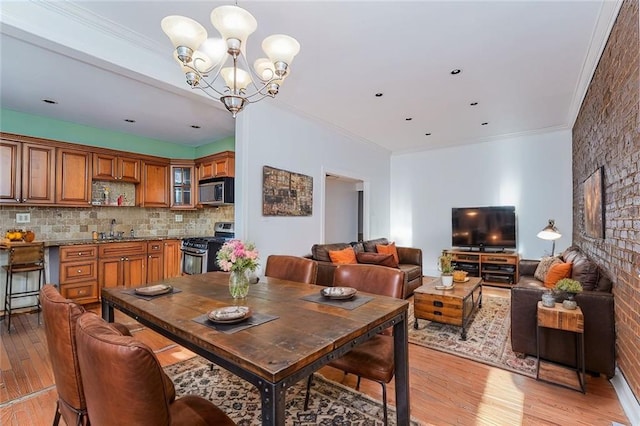 dining area featuring sink, light wood-type flooring, ornamental molding, and an inviting chandelier