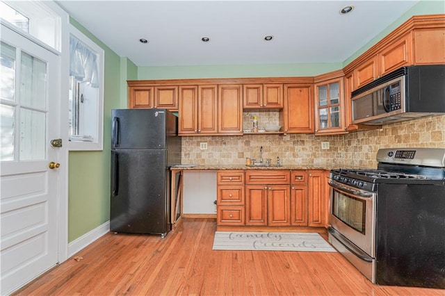 kitchen with sink, decorative backsplash, appliances with stainless steel finishes, light hardwood / wood-style floors, and light stone counters