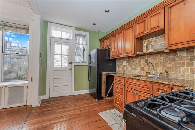 kitchen with light stone counters, a wealth of natural light, black appliances, and sink