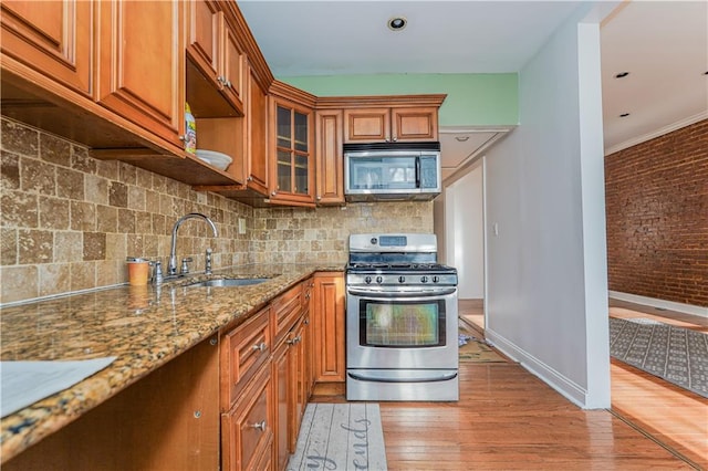 kitchen featuring light stone countertops, sink, brick wall, backsplash, and appliances with stainless steel finishes