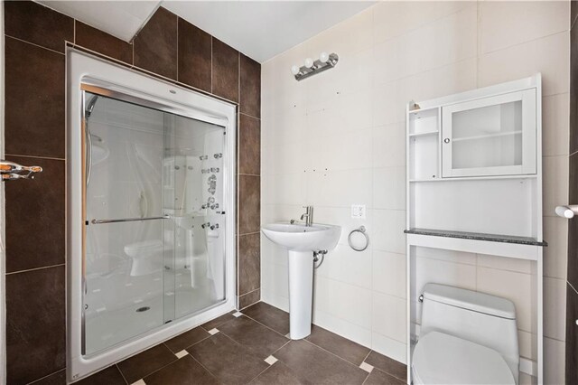 bathroom featuring walk in shower, tile patterned flooring, tile walls, and toilet