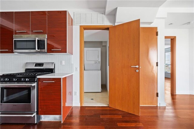 kitchen featuring backsplash, dark hardwood / wood-style floors, stacked washer / dryer, and stainless steel appliances