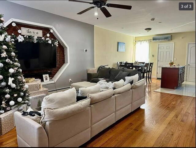 living room featuring a wall unit AC, ceiling fan, wood-type flooring, and a baseboard heating unit