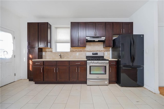 kitchen with stainless steel range with gas cooktop, light countertops, backsplash, freestanding refrigerator, and under cabinet range hood