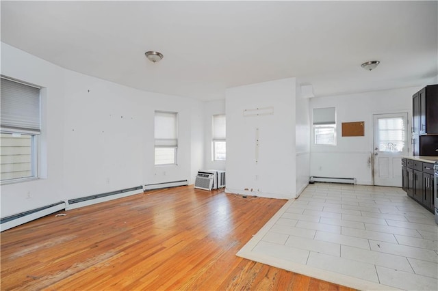 unfurnished living room featuring light wood-type flooring, a wall mounted air conditioner, a sink, and baseboard heating