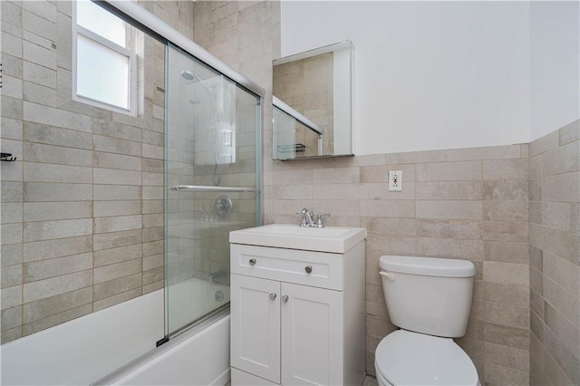 bathroom featuring bath / shower combo with glass door, vanity, toilet, and tile walls