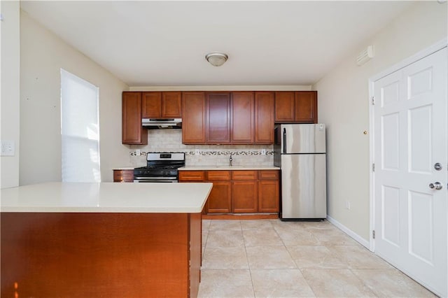 kitchen with tasteful backsplash, brown cabinetry, appliances with stainless steel finishes, light countertops, and under cabinet range hood