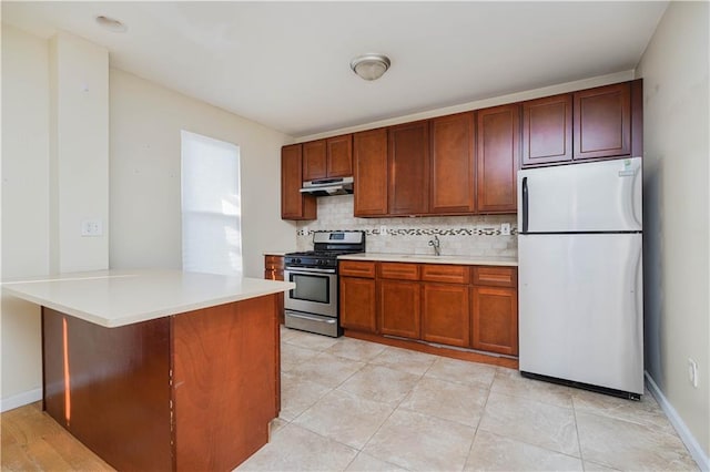 kitchen with tasteful backsplash, a peninsula, stainless steel appliances, light countertops, and under cabinet range hood