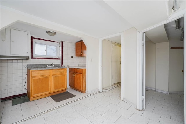 kitchen with brown cabinets, tile walls, light floors, light countertops, and backsplash