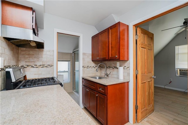 kitchen featuring reddish brown cabinets, light wood-style floors, a sink, ceiling fan, and stainless steel gas range oven