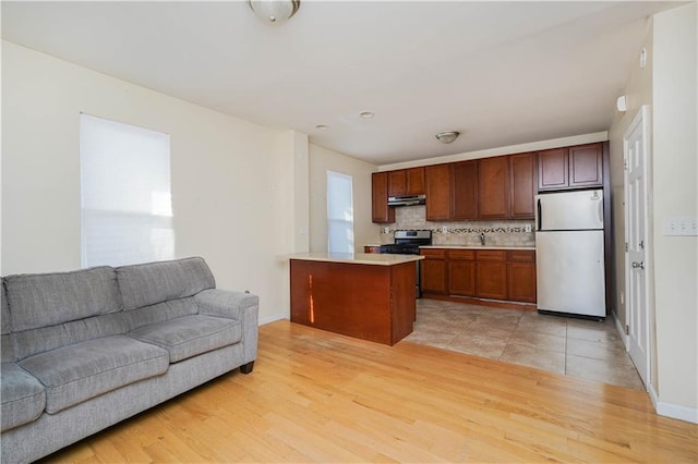 kitchen featuring light wood-style flooring, under cabinet range hood, open floor plan, light countertops, and appliances with stainless steel finishes