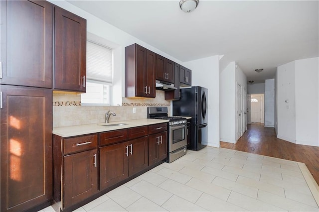 kitchen featuring under cabinet range hood, a sink, light countertops, freestanding refrigerator, and stainless steel range with gas stovetop