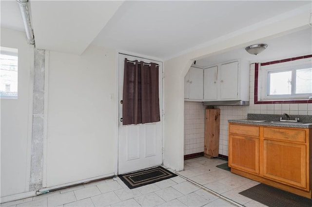 kitchen with light tile patterned floors, a sink, backsplash, brown cabinets, and dark countertops