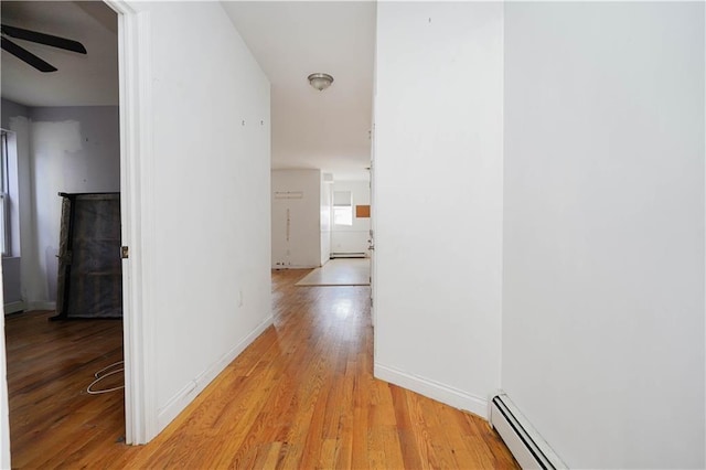 corridor featuring a baseboard heating unit, light wood-type flooring, a baseboard radiator, and baseboards