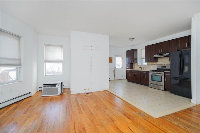 kitchen featuring under cabinet range hood, dark brown cabinets, stainless steel gas range, freestanding refrigerator, and a wall mounted air conditioner