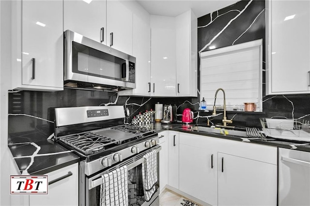 kitchen featuring appliances with stainless steel finishes, dark countertops, a sink, and white cabinets