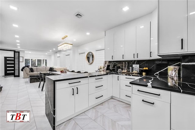 kitchen with white cabinetry, backsplash, kitchen peninsula, and dark stone countertops