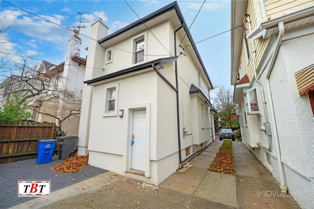 rear view of property with a chimney, fence, and stucco siding