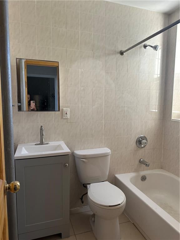 full bathroom featuring vanity, tile patterned floors, tiled shower / bath combo, toilet, and tile walls