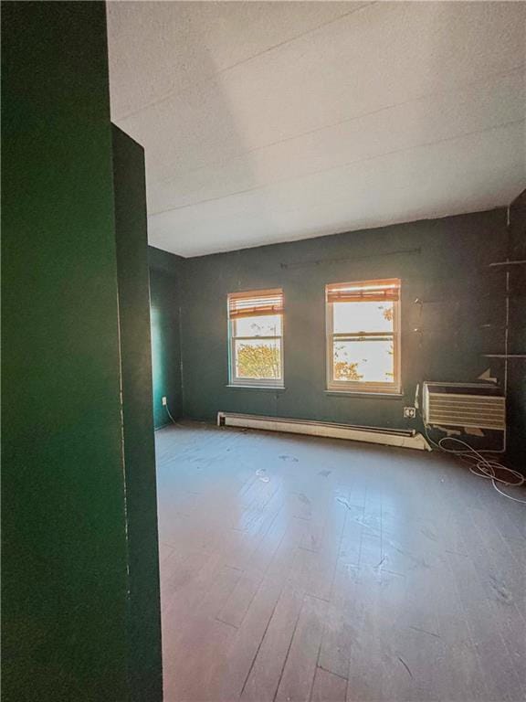 unfurnished room with a textured ceiling, a wall unit AC, wood finished floors, and a baseboard radiator