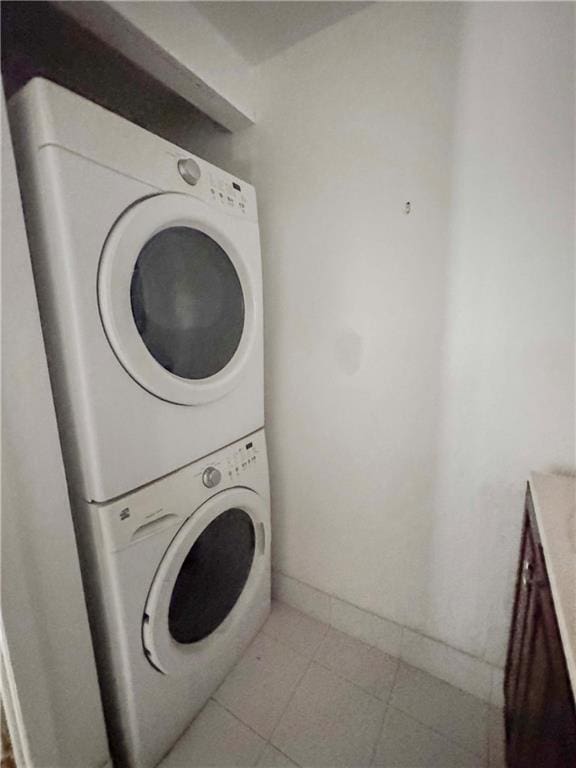 laundry area featuring light tile patterned floors, laundry area, stacked washer and clothes dryer, and baseboards