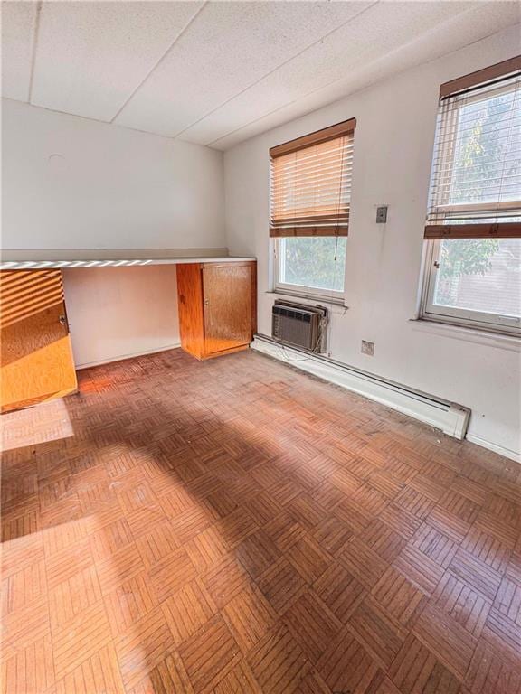 unfurnished living room featuring light parquet floors, a drop ceiling, and a baseboard radiator