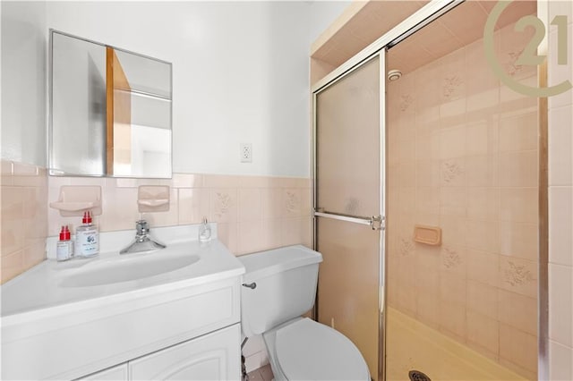 bathroom with a shower with door, vanity, tile walls, and toilet