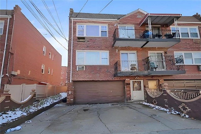 view of property featuring driveway, a balcony, an attached garage, fence, and brick siding