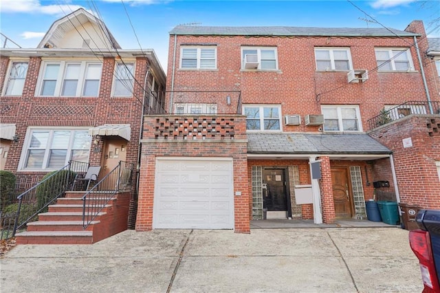 view of property with driveway, brick siding, a wall mounted AC, and an attached garage