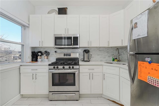 kitchen with appliances with stainless steel finishes, white cabinets, light countertops, and a sink