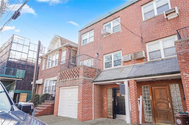 townhome / multi-family property featuring a garage, cooling unit, a wall mounted air conditioner, and brick siding